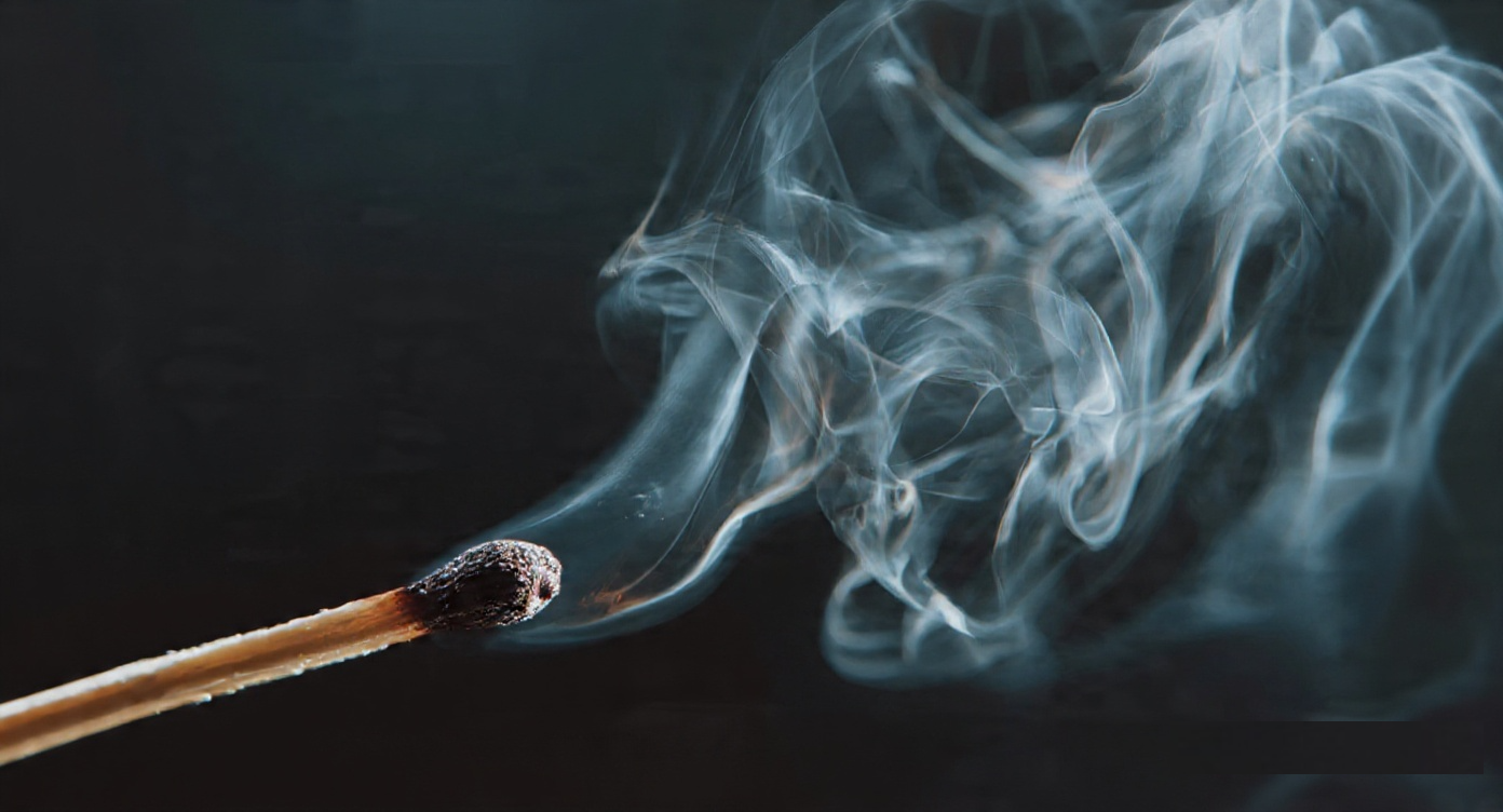 A spent matchbook resting in shadow, sulfur smoke curling upward